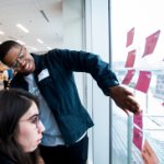 Students add sticky notes to a window during a design thinking workshop on December 11, 2020